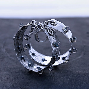 Puede incluir: Una pulsera de plata con textura martillada, con múltiples bandas conectadas por una cadena. La pulsera está adornada con pequeñas piedras preciosas transparentes. El diseño es intrincado y el metal tiene un acabado ligeramente oscurecido.