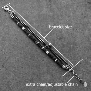 May include: A silver bracelet with two strands. One strand has small, round beads, and the other has black cylindrical beads with silver accents. An extra chain allows for an adjustable fit.