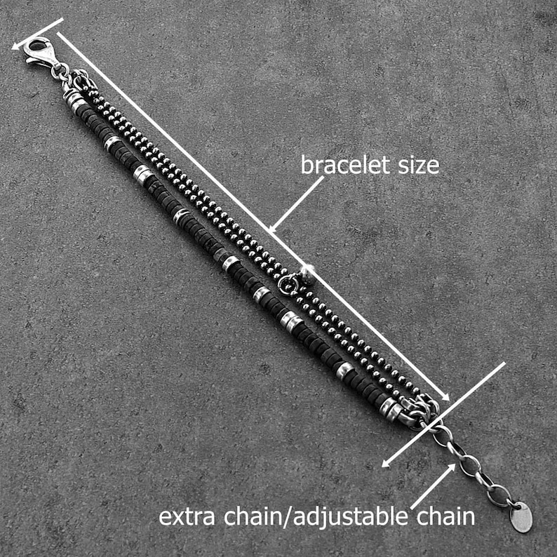 May include: A silver bracelet with two strands. One strand has small, round beads, and the other has black cylindrical beads with silver accents. An extra chain allows for an adjustable fit.