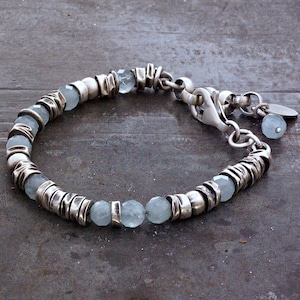May include: A silver bracelet featuring light blue gemstone beads and textured silver links. The bracelet has a lobster clasp closure and a small charm with a matching bead. The bracelet is approximately 7 inches in length.