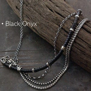 Op de afbeelding: Een meerstrengs ketting met een zilveren ketting, een streng zwarte onyx kralen met zilveren tussenstukjes, een fijne schakelketting en een zilveren kralenketting. De tekst Black Onyx is zichtbaar aan de linkerkant van de afbeelding.