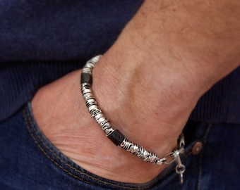 Op de afbeelding: Een zilveren armband met zwarte kralen en een zilveren sluiting. De armband zit om de pols van een persoon.
