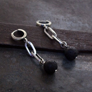 以下が含まれることがあります： 銀製のフープピアス。各フープから黒い溶岩ビーズがぶら下がっています。ピアスは銀のチェーンでビーズに繋がっています。