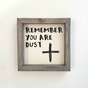 Pode incluir: Uma placa enquadrada com o texto "Remember You Are Dust" e um sinal de mais preto desenhado em um fundo branco. A moldura é de madeira cinza.
