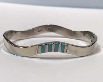 May include: A silver-toned bracelet with a wavy design. The bracelet features a series of rectangular turquoise-colored inlays. The bracelet is a piece of jewelry.