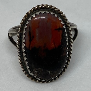 May include: A silver ring with a brown, red, and white oval stone set in a rope-like border.