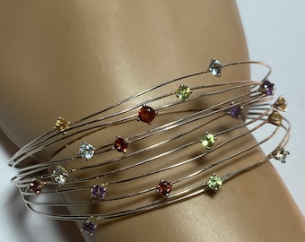 May include: A silver bracelet with multiple strands and colorful gemstones. The bracelet features a variety of colors, including red, orange, yellow, green, blue, and purple.