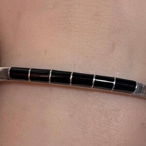 May include: A silver cuff bracelet with a series of six rectangular black onyx stones. The bracelet is worn on a wrist, showcasing the contrast between the shiny metal and the dark stones. A simple, elegant piece of jewelry.