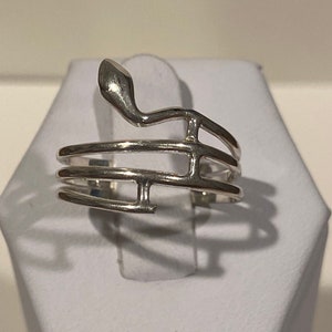 May include: A silver ring featuring a treble clef design. The ring is crafted from three interwoven bands of metal.