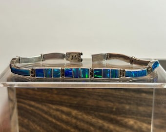 May include: Silver bracelet featuring rectangular blue opal stones. The bracelet has a classic design with a secure clasp. The opal stones display a vibrant play of color, ranging from deep blues to hints of green.