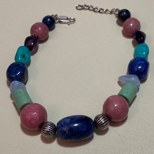 May include: A multi-coloured beaded bracelet with a silver clasp. The beads are made of various stones, including turquoise, lapis lazuli, amethyst, and rose quartz.