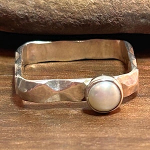 May include: A silver ring with a hammered texture and a white pearl gemstone.