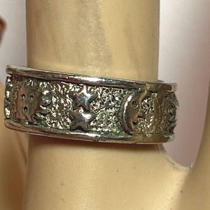 May include: A silver ring with a textured surface and a design of stars, moons, and other celestial bodies.