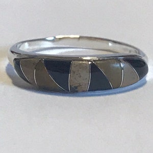 May include: A silver band ring with a black and white inlay design. The inlay is made of different materials, including black onyx and white stone.