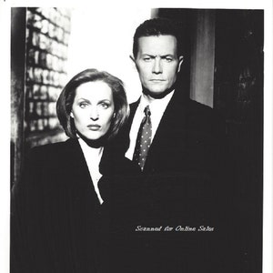 May include: Black and white photo of two people in suits. The woman is on the left and the man is on the right. The woman has short, dark hair and is wearing a black suit. The man has short, dark hair and is wearing a black suit with a white shirt and a patterned tie. The photo is against a brick wall background. The text "Scanned for Online Sales" is at the bottom of the photo.