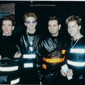 May include: Five individuals wearing black leather-style jackets with horizontal reflective silver or orange strips. The jackets feature high collars and long sleeves. Some individuals wear silver chain necklaces and tinted glasses. The text Scanned for Online Sales is visible at the top.