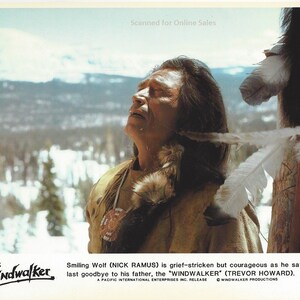 May include: A vintage film still featuring a person with long dark hair wearing a tan buckskin garment with a beaded medallion. The text reads: Windwalker, Smiling Wolf (NICK RAMUS) is grief-stricken but courageous as he says his last goodbye to his father, the WINDWALKER (TREVOR HOWARD). A PACIFIC INTERNATIONAL ENTERPRISES INC. RELEASE © WINDWALKER PRODUCTIONS.