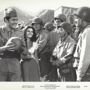 May include: Black and white photo of a group of soldiers in uniform. A man in a military uniform is holding a helmet and smiling at a woman in a white dress. The text "WHAT DID YOU DO IN THE WAR DADDY?" is printed at the bottom of the photo.