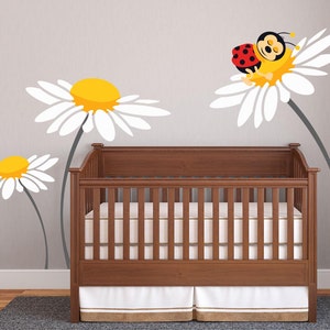 May include: A wooden cot with a white mattress and a white frilled skirt. The cot is decorated with a wall decal of a ladybug sleeping on a daisy.
