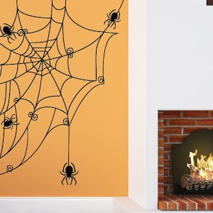 May include: A black spider web decal with multiple spiders on an orange wall. The web is hanging from the ceiling and has a fireplace in the background.