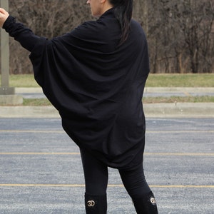 May include: A black long-sleeved shirt with a draped, oversized design. The shirt is worn with black leggings and black boots.