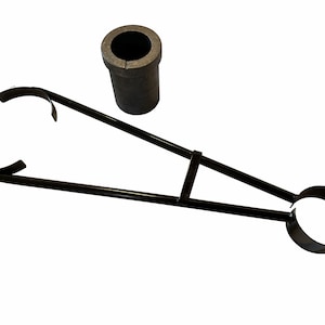 May include: Black metal tongs with a large circular opening at one end and a smaller opening at the other. The tongs are used to hold a gray ceramic crucible.