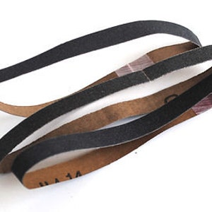 May include: Three black sanding belts with brown backing. The belts are folded and stacked on top of each other. The text "UA 14" is visible on the bottom belt.