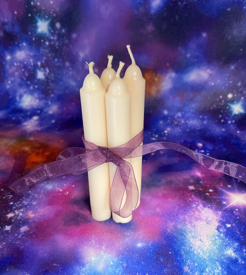 Peut inclure: Un lot de quatre bougies effil&eacute;es blanc cass&eacute; attach&eacute;es ensemble par un ruban violet transparent. Chaque bougie pr&eacute;sente un sommet arrondi et une m&egrave;che en coton. Les bougies sont dispos&eacute;es verticalement en groupe, maintenues par le ruban.