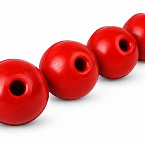 Könnte beinhalten: Vier leuchtend rote, kugelförmige Objekte, die in einer diagonalen Linie angeordnet sind. Jeder glatte, runde Gegenstand weist eine einzelne, mittig platzierte kreisförmige Öffnung auf der Oberseite auf, was ein einheitliches Bild ergibt.