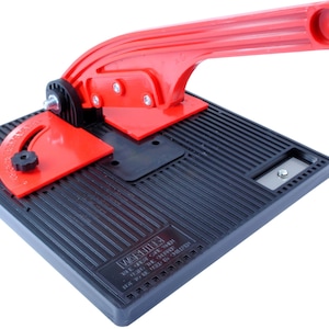 May include: A red and black tile cutter with a handle and a protractor. The base of the cutter has a textured surface and the text "WARNING! USE GREAT CARE WHEN USING THIS TOOL. IT MAY BE SHARP. KEEP OUT OF REACH OF CHILDREN." is printed on the base.