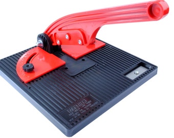May include: A red and black tile cutter with a handle and a protractor. The base of the cutter has a textured surface and the text "WARNING! USE GREAT CARE WHEN USING THIS TOOL. IT MAY BE SHARP. KEEP OUT OF REACH OF CHILDREN." is printed on the base.