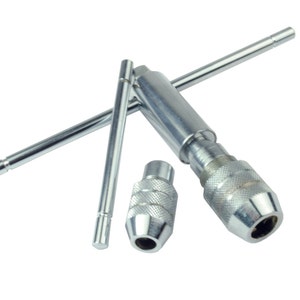 Peut inclure: Ensemble d'outils en métal argenté, dont un porte-taraud et deux mandrins, sur fond blanc. Le porte-taraud a une poignée et une forme en T. Les mandrins sont cylindriques avec des poignées texturées.