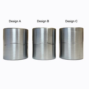 Könnte beinhalten: Drei silberne Metallzylinder mit unterschiedlichen Designs am oberen Rand. Die Zylinder sind mit "Design A", "Design B" und "Design C" beschriftet.