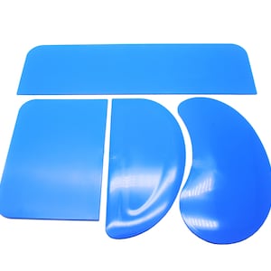 May include: A set of four blue plastic cake decorating tools. The set includes a long rectangular spatula, a smaller rectangular spatula, a curved spatula, and a crescent-shaped spatula.