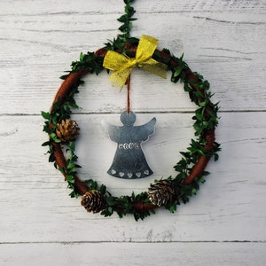 May include: A brown wreath with green leaves and a yellow bow. A silver angel ornament with the word "HOPE" hangs from the bow.