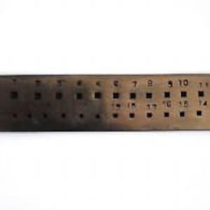 May include: A metal ruler with numbered holes, ranging from 1 to 17, for measuring the size of jewellery or other small objects.