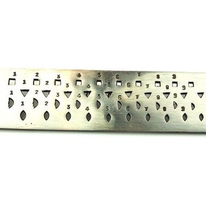 May include: A silver metal gauge with a series of holes in different shapes and sizes. The gauge is labelled "STELLA" and has numbers 1 through 9 along the top.