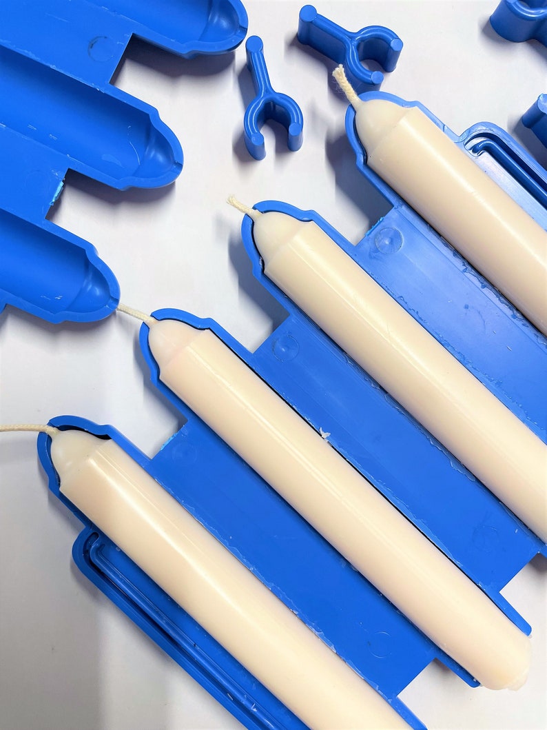 Peut inclure: Un moule &agrave; bougie en plastique bleu contenant trois bougies effil&eacute;es blanc cass&eacute; avec des m&egrave;ches visibles. Le moule est compos&eacute; de sections cylindriques reli&eacute;es avec de petits clips en plastique bleu pour fixer les deux moiti&eacute;s du moule.