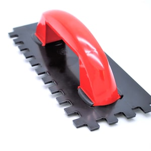 May include: A red plastic handle attached to a black metal notched trowel. The trowel is used for spreading mortar or grout.