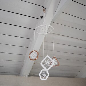 May include: White dreamcatchers of various sizes and shapes hang from a white wooden ceiling. The dreamcatchers are made of white string and have brown wooden beads.