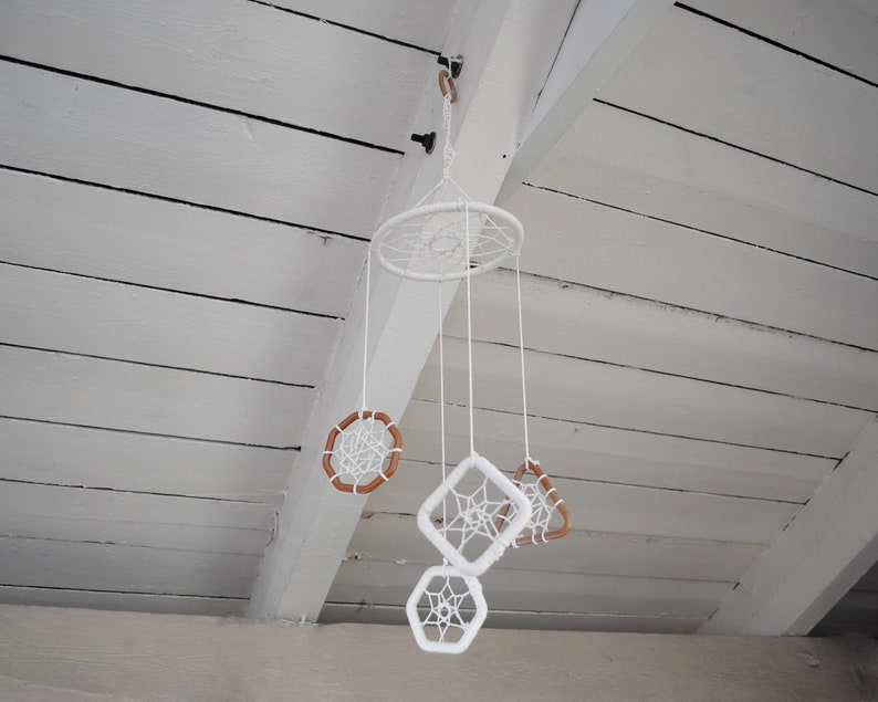 May include: White dreamcatchers of various sizes and shapes hang from a white wooden ceiling. The dreamcatchers are made of white string and have brown wooden beads.