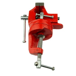 May include: A red metal bench vise with a silver handle and a silver screw. The vise is mounted on a base with a clamp.