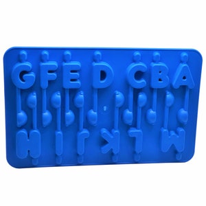 K&ouml;nnte beinhalten: Eine leuchtend blaue Silikonform mit den Buchstaben A bis W. Die Buchstaben sind mit Designs in Form von Noten verbunden. Die Form ist f&uuml;r die Herstellung von Eisw&uuml;rfeln, Pralinen oder anderen Leckereien konzipiert.