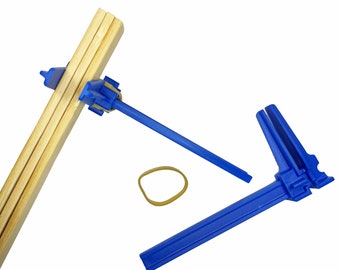 May include: Two blue plastic clamps for woodworking, one clamping a stack of wooden boards, the other lying flat. A yellow rubber band is also shown.