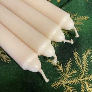 Peut inclure: Un ensemble de quatre bougies effil&eacute;es cylindriques et lisses de couleur blanc cass&eacute;, dispos&eacute;es en rang&eacute;e parall&egrave;le. Chaque bougie pr&eacute;sente un sommet arrondi avec une courte m&egrave;che en coton blanc visible au centre. La cire est opaque.