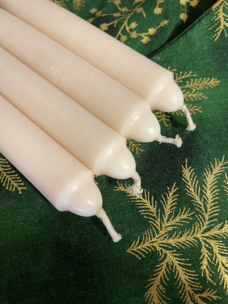 Peut inclure: Un ensemble de quatre bougies effil&eacute;es cylindriques et lisses de couleur blanc cass&eacute;, dispos&eacute;es en rang&eacute;e parall&egrave;le. Chaque bougie pr&eacute;sente un sommet arrondi avec une courte m&egrave;che en coton blanc visible au centre. La cire est opaque.