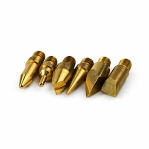 May include: A set of six brass-coloured metal tips with threaded ends, featuring various pointed, conical, and flat-edged shapes. These components have a metallic finish and are arranged in a row, showcasing distinct geometric profiles for precision work.