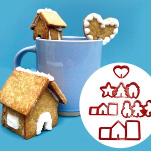 May include: A set of red plastic cookie cutters shaped like a heart, star, Christmas tree, house, snowman, and gingerbread people. The cutters are on a white background.