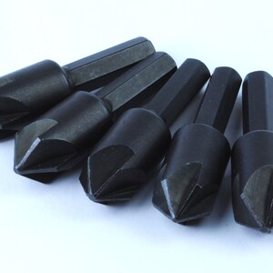 May include: Five black drill bits with a pointed tip and a hexagonal shank.
