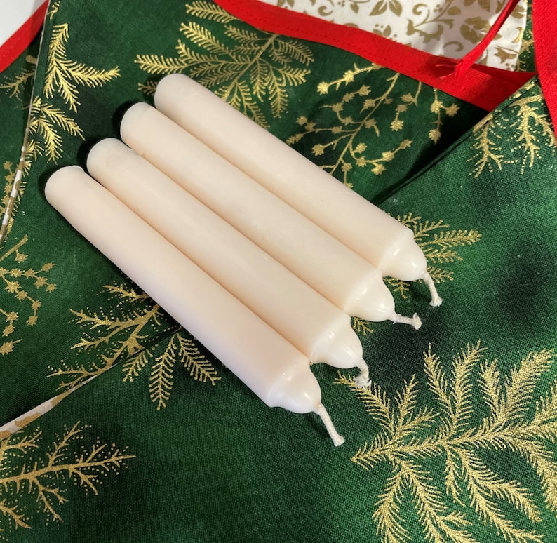 Peut inclure: Quatre bougies cylindriques blanc cass&eacute; avec des sommets arrondis et des m&egrave;ches en coton visibles. Les bougies sont dispos&eacute;es en rang&eacute;e parall&egrave;le, chacune pr&eacute;sentant une surface en cire lisse et solide. Elles sont pos&eacute;es sur un tissu vert fonc&eacute;.
